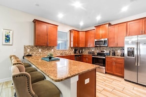 A modern kitchen with wooden cabinets, granite countertops, stainless steel appliances, and a built-in island with bar seating. - No Rear Neighbors • South-Facing Pool & Spa • Game Room • Lazy River • Disney (Davenport)