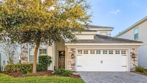 A single-story house with a stone facade, a tiled roof, and a white garage door. - Pool & Spa | Gameroom | Waterpark near Disney 1538 (Davenport)