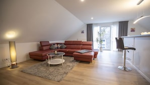 A modern living room with a red sofa, a coffee table, and a bar area with a stool. - Vacation apartment Peters Goslar, Sudmerberg 85 sqm (Goslar)