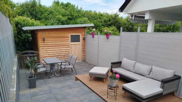 A patio with a wooden table and chairs, a sofa, and a small garden area with potted plants. - Vacation apartment Peters Goslar, Sudmerberg 85 sqm (Goslar)