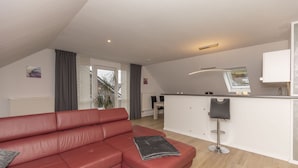 A modern living room with a red leather sofa, a small bar area, and a view of the outdoors. - Vacation apartment Peters Goslar, Sudmerberg 85 sqm (Goslar)