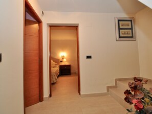 A hallway with a wooden door, a bedside table with a lamp, and a staircase leading to another room.