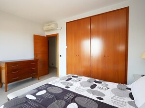 A bedroom with a bed, a wooden wardrobe, a dresser, and an air conditioning unit.