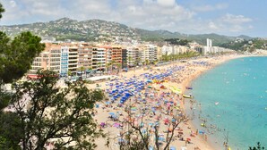 A beach with numerous umbrellas and people, a row of multi-story buildings, and a clear blue sea. - Spacious apartment 8 people, sea view terrace, Lloret de Mar (Lloret de Mar)