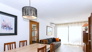 A dining area with a wooden table and chairs, a sofa with cushions, a decorative hanging light, and a framed picture on the wall. - Spacious apartment 8 people, sea view terrace, Lloret de Mar (Lloret de Mar)