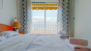 A hotel room with a bed, a nightstand, a lamp, and a view of the sea through a balcony. - Spacious apartment 8 people, sea view terrace, Lloret de Mar (Lloret de Mar)