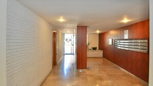 Un pasillo con una pared de ladrillo blanco en un lado y paneles de madera en el otro, que conduce a una zona de recepción con una planta y un mostrador con llaves.