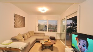 A living room with a sofa, a coffee table, a television, and a large window.