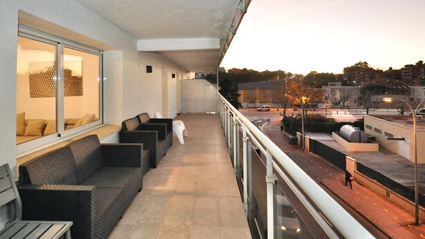 A balcony with a sofa and chairs, a view of the street, and a building in the background.
