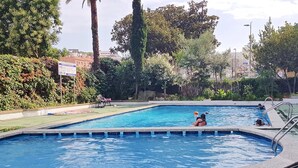 A swimming pool with a surrounding garden and a bench.