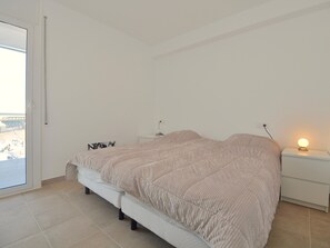 Une chambre à coucher avec un lit, une table de chevet, une lampe et une vue sur l’extérieur, visible à travers une porte.