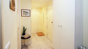 A hallway with a tiled floor, a small table with a plant and a basket, a framed picture on the wall, and a door at the end.