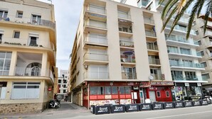 A multi-story building with balconies, a red storefront with a sign that reads "BAR" and "DINER," and a row of black advertising boards with the text "Iloret de mar."