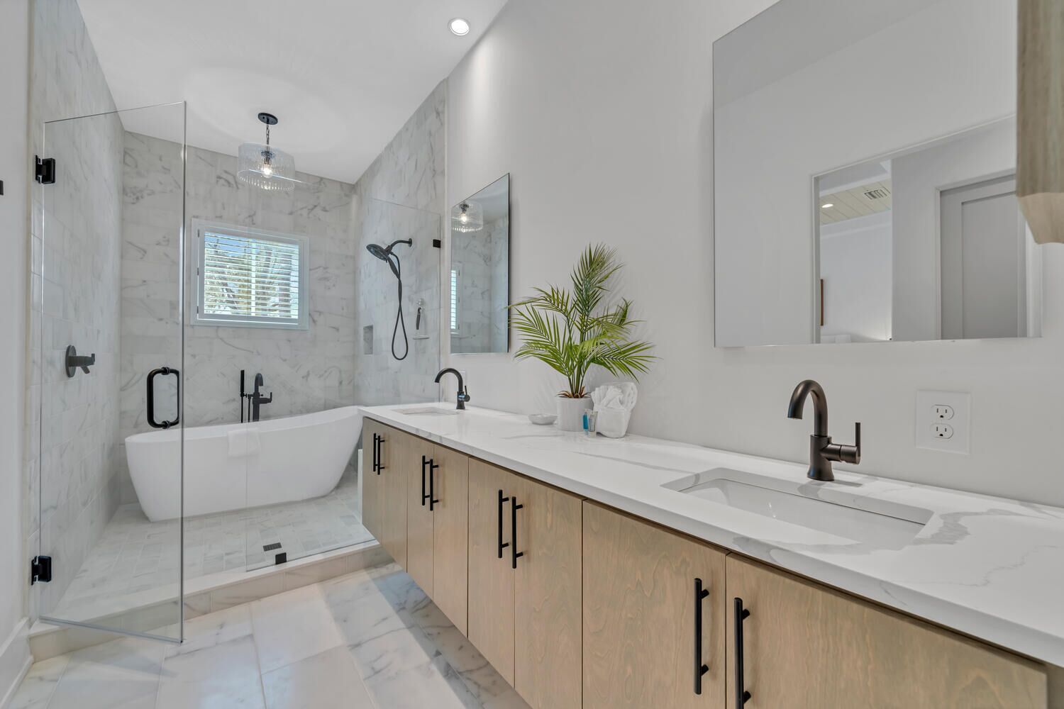 A modern bathroom with a glass-enclosed shower, a freestanding bathtub, a vanity with a sink, and a large mirror.