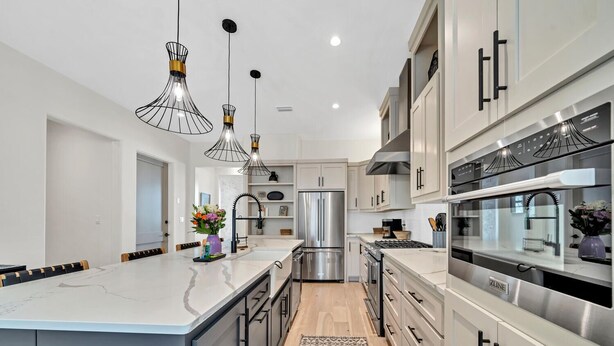 A modern kitchen with a large island, stainless steel appliances, and pendant lighting.