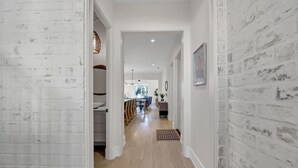 A hallway with white brick walls, wooden flooring, and a dining area in the background.
