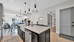 A modern kitchen with a central island, pendant lighting, and a view into the dining area.