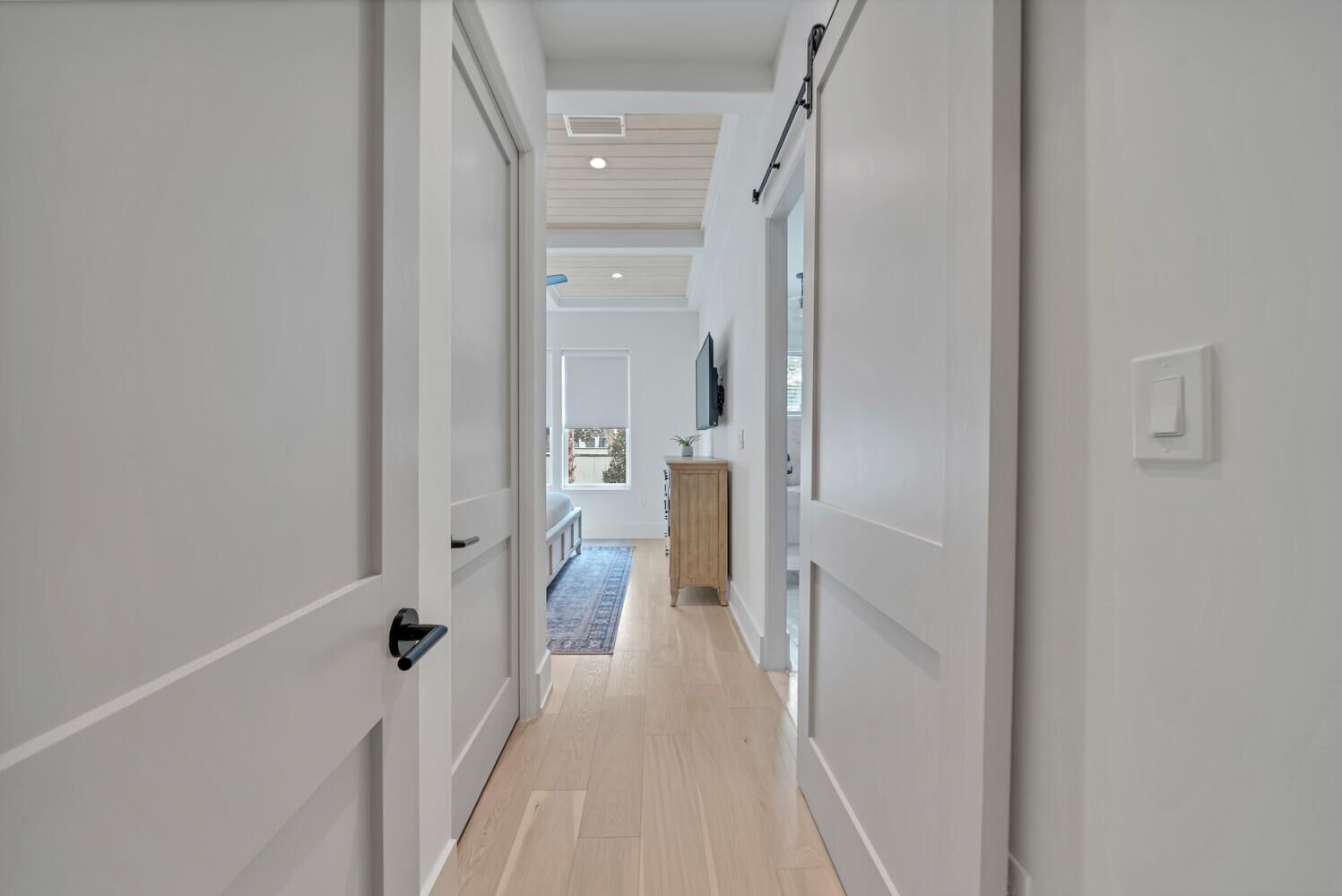 A hallway with white walls, a wooden floor, and a door on the left.
