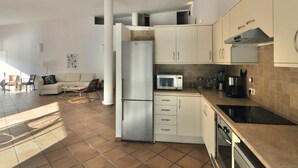 A modern kitchen with white cabinets, a stainless steel refrigerator, a microwave, and a coffee maker. There is a dining area with a sofa and chairs. - Spacious Villa with Private Pool & BBQ, Near Lloret de Mar (Lloret de Mar)