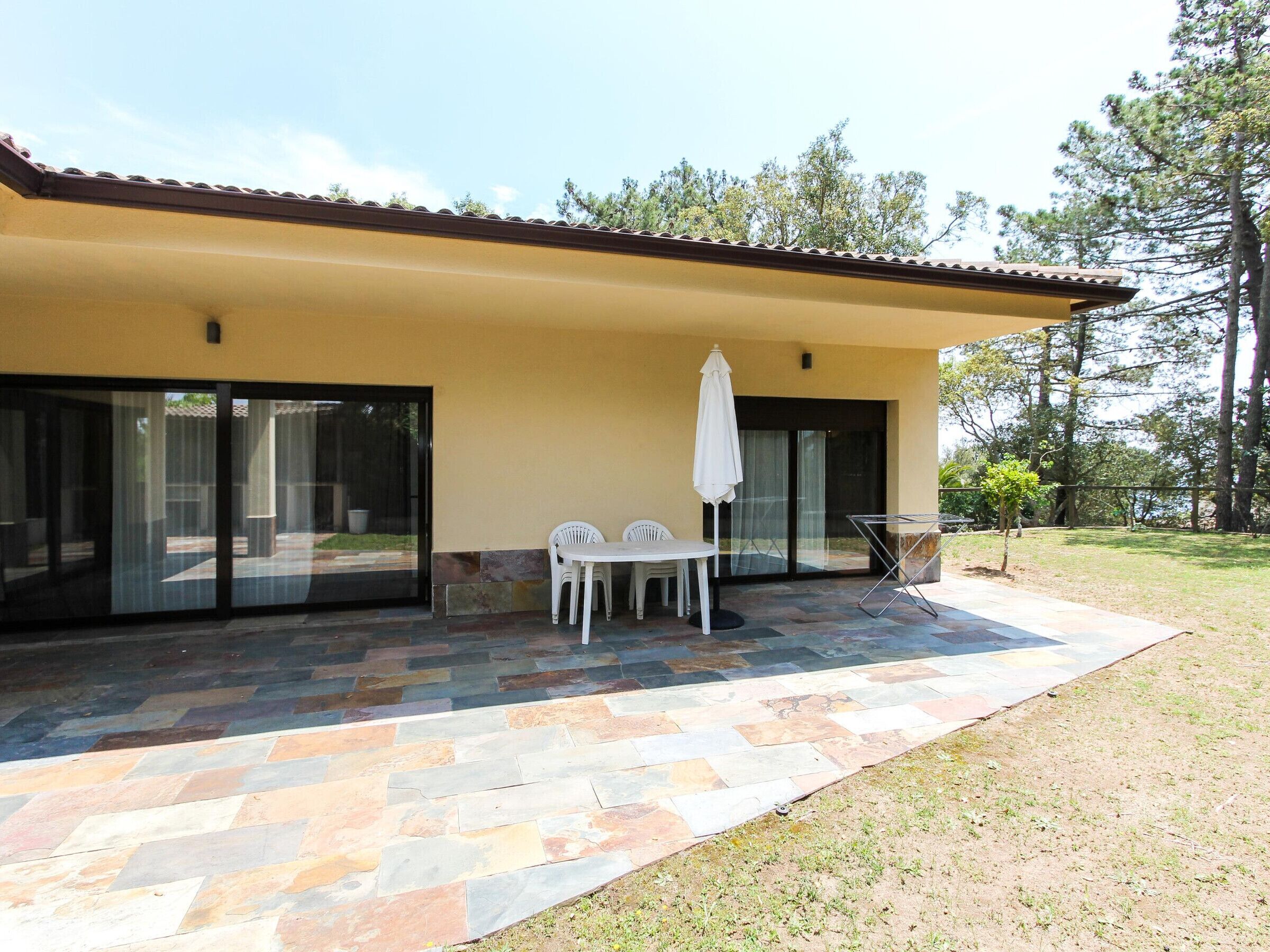 A house with a patio area featuring a stone floor, a table with chairs, and a white umbrella.