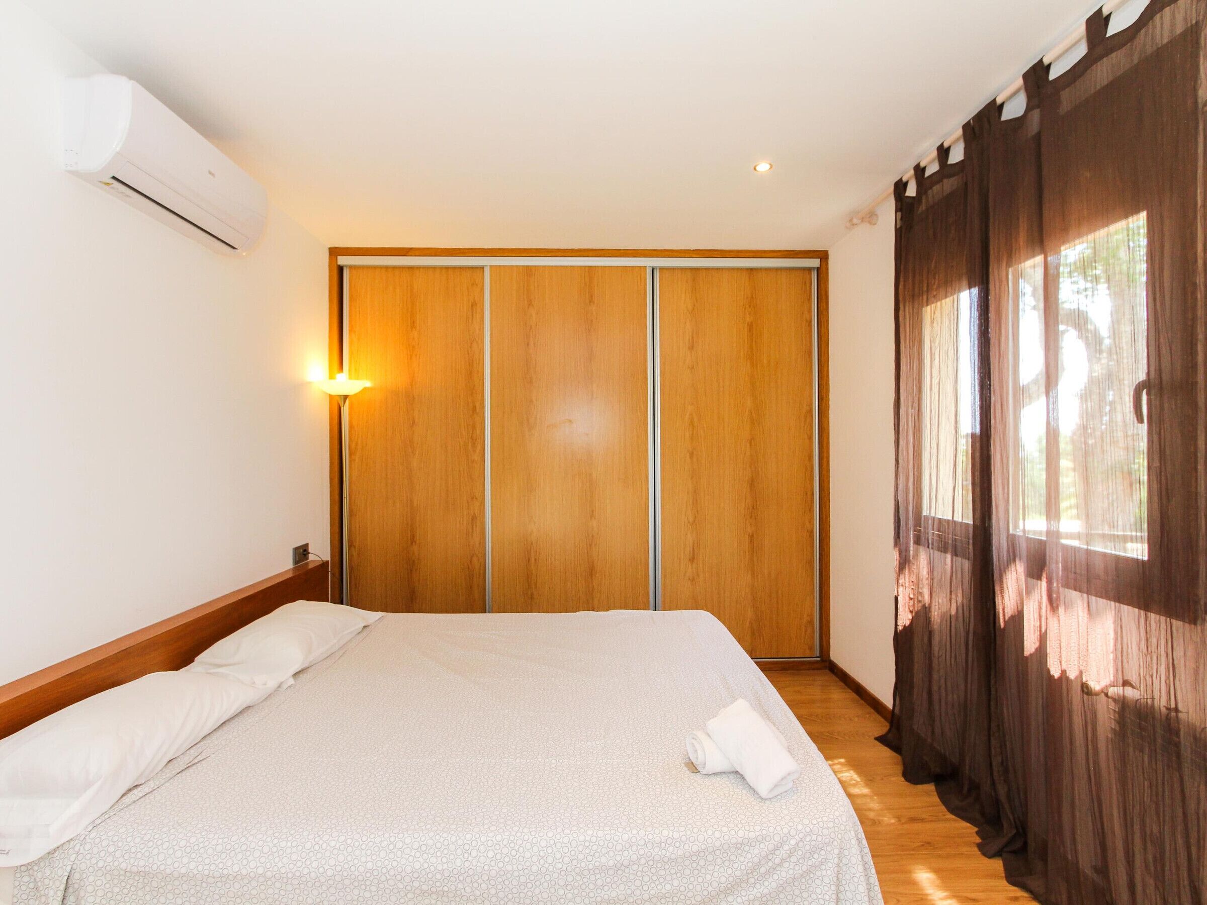 A bedroom with a bed, a wardrobe, a bedside lamp, and a window with curtains.