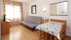 Ett rum med en soffa, ett matbord med stolar, en lampa, en inramad tavla och en spegel på väggen.