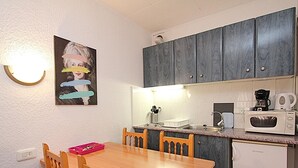 Ett kompakt kök med ett träbord och stolar, en mikrovågsugn, en kaffebryggare och skåp ovanför bänkskivan.