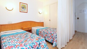 A hotel room with two beds, a wooden headboard, a framed picture on the wall, and a white door with a phone.