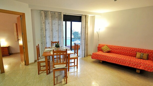 A dining area with a table and chairs, a sofa, and a window with curtains.