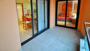 A balcony with a dining area and a bedroom visible through a sliding door.