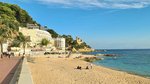 Una playa con un hotel llamado 'Hotel Rosamar Maximo' y un restaurante de pizza 'PIZZA POMODORO' a la izquierda.