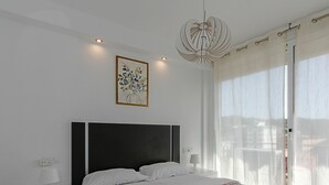 Un dormitorio moderno con una cama grande, una mesita de noche, una lámpara, una luz de techo y una ventana con cortinas.