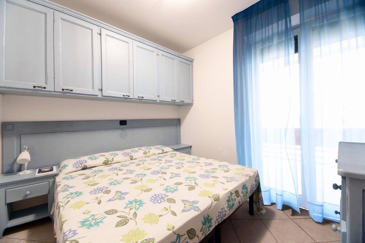 A bedroom with a bed, a nightstand, a dresser, and a window with curtains.