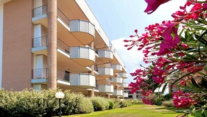 A multi-story building with balconies, surrounded by greenery and flowers.