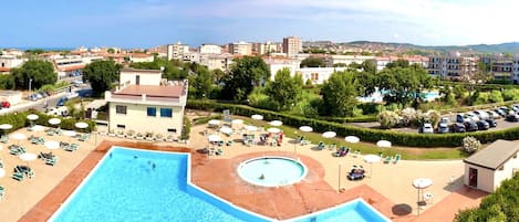 A resort with a large pool, sun loungers, and a view of the surrounding cityscape.
