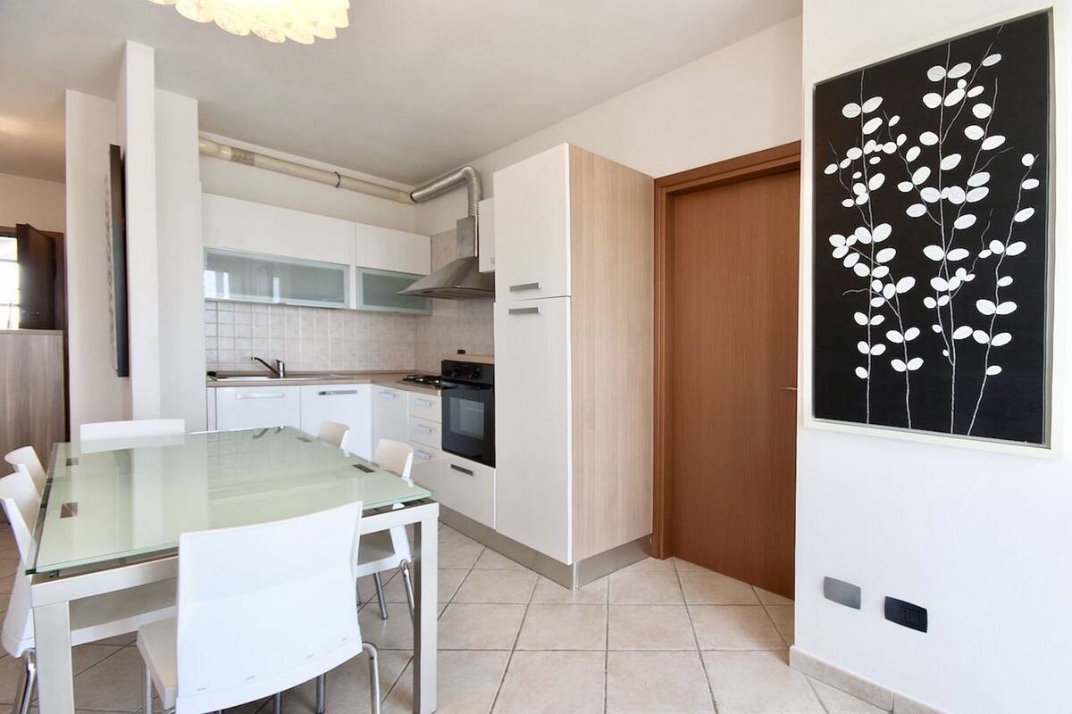 A modern kitchen with white cabinetry, a glass dining table, and a black and white wall art piece.