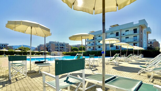 A poolside area with lounge chairs and umbrellas, a clear sky, and a building in the background.