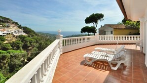 A balcony with white chairs and a view of a coastal landscape.