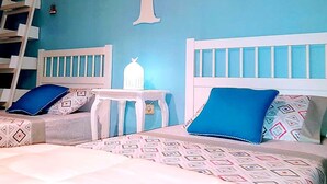 Een slaapkamer met twee bedden, elk voorzien van een witte hoofdbord en blauwe kussens. Er staat een klein wit tafeltje met een lamp tussen de bedden.