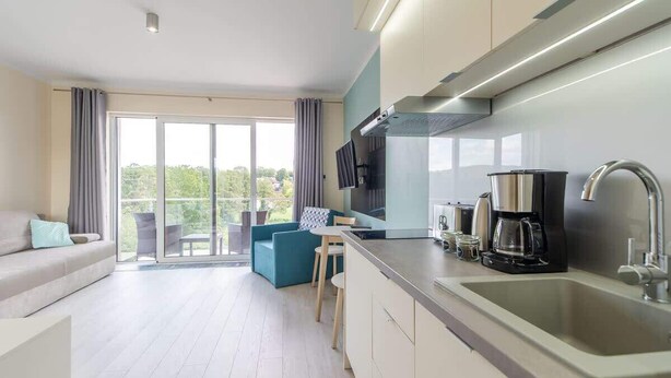 A modern kitchen with a large island, built-in appliances, and a view through the glass doors. - Comfortable Studio | Parking, Balcony, Close to the Beach (Miedzyzdroje)