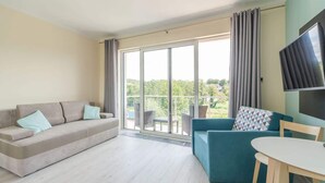 A modern living room with a sofa, a smaller blue sofa, a table, and a TV. - Comfortable Studio | Parking, Balcony, Close to the Beach (Miedzyzdroje)