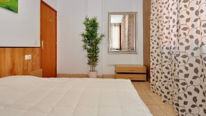Una camera da letto con un letto, una pianta in vaso, uno specchio, un armadietto in legno e una tenda decorata.
