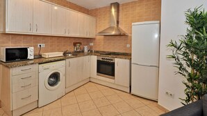 Una cucina compatta con mobili in legno chiaro, un forno a microonde, una lavatrice, un fornello e un frigorifero.
