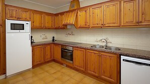 A kitchen with wooden cabinets, a microwave, a sink, and a dishwasher. - 6-Bedroom Villa with Private Pool in Lloret de Mar (Lloret de Mar)