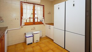 A kitchen with a refrigerator, a window with curtains, a radiator, and a trash bin. - 6-Bedroom Villa with Private Pool in Lloret de Mar (Lloret de Mar)