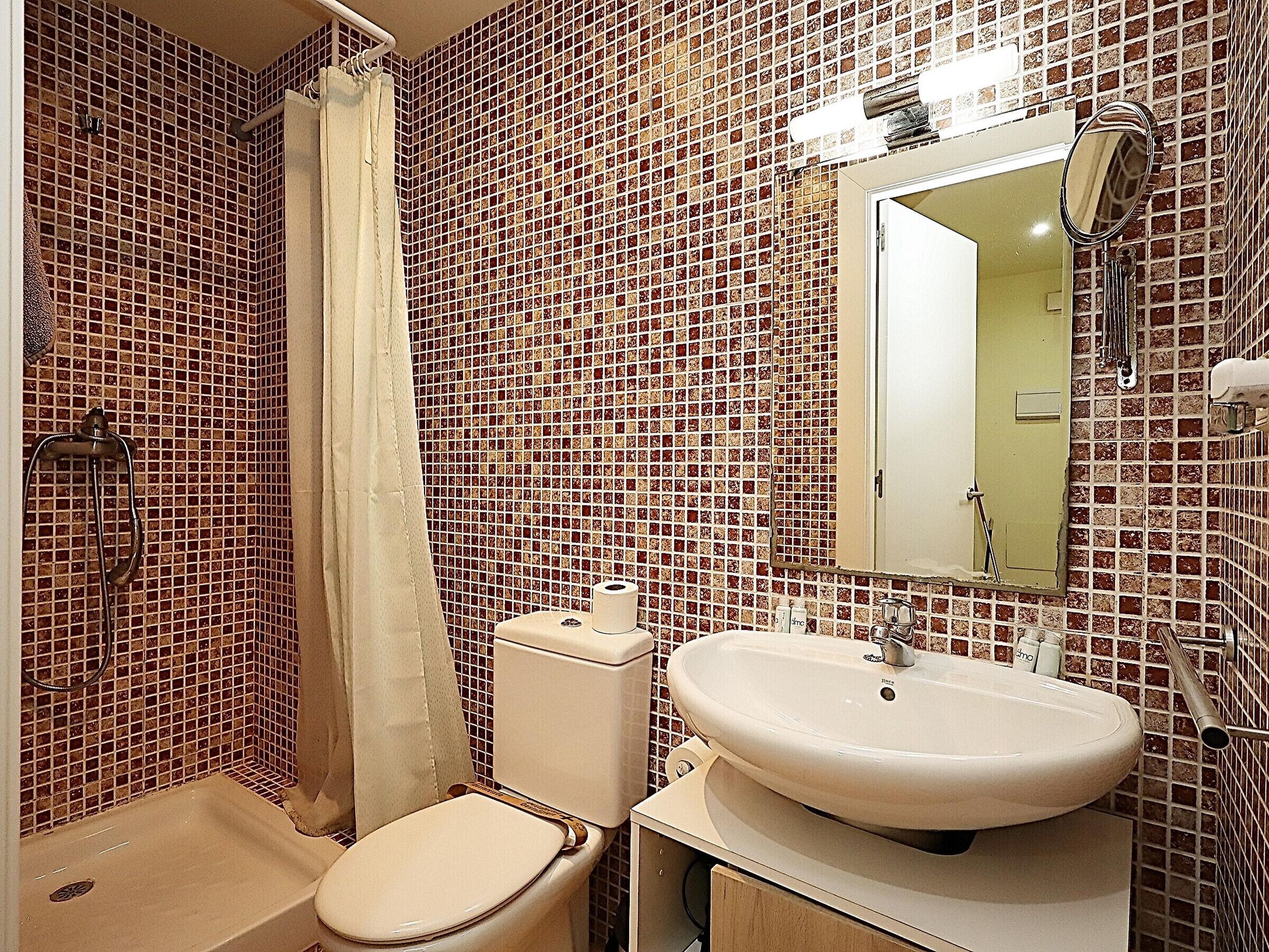 Ein Badezimmer mit gefliesten Wänden, Toilette, Waschbecken und Dusche.
