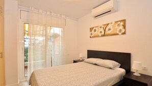 A bedroom with a bed, a nightstand, a wall-mounted air conditioner, and a window with curtains. - Cozy Apartment with Pool, 150m from Beach - Lloret de Mar (Lloret de Mar)