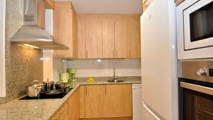 A compact kitchen with wooden cabinets, a built-in oven, and a microwave. - Cozy Apartment with Pool, 150m from Beach - Lloret de Mar (Lloret de Mar)
