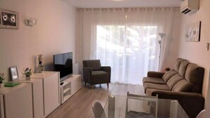 A living room with a television, a sofa, a chair, and a glass coffee table. - Cozy Apartment with Pool, 150m from Beach - Lloret de Mar (Lloret de Mar)
