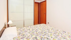 A bedroom with a bed, a nightstand, a lamp, a wardrobe with a mirror, and a door. - Cozy Apartment with A/C, 150m from Lloret de Mar Beach (Lloret de Mar)